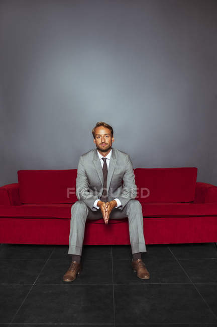 Portrait of businessman wearing grey suit sitting with hands clasped in dark room — Stock Photo