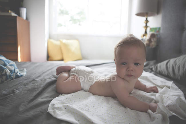 Portrait of little baby lying on front on spotted cloth with raised head — Stock Photo
