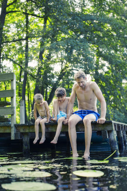 Батько і сини лякають ноги в озері разом — стокове фото