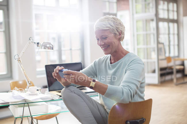 Деловая женщина, использующая мобильный телефон на столе домашнего офиса — стоковое фото
