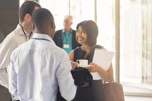 Donna d'affari che parla con colleghi che detengono una tazza di caffè in carica — Foto stock