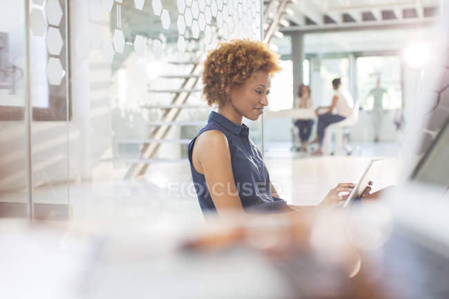 Жінка використовує цифровий планшет в офісі, колеги на задньому плані — стокове фото