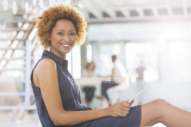 Portrait of smiling woman using digital tablet in office corridor, colleagues in background — Stock Photo