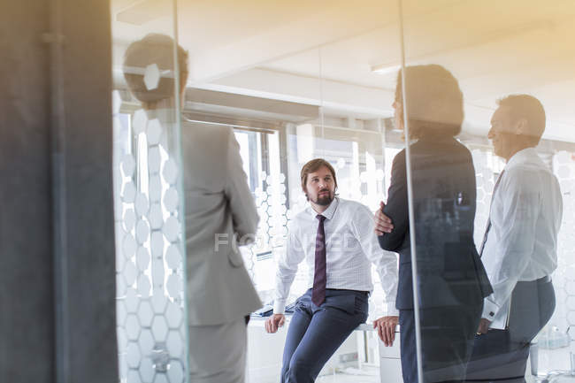 Personas que se reúnen en una oficina moderna vista a través de una puerta de vidrio - foto de stock