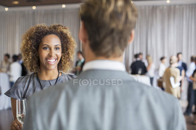 Two business people standing with champagne flutes, smiling and talking in conference room — Stock Photo