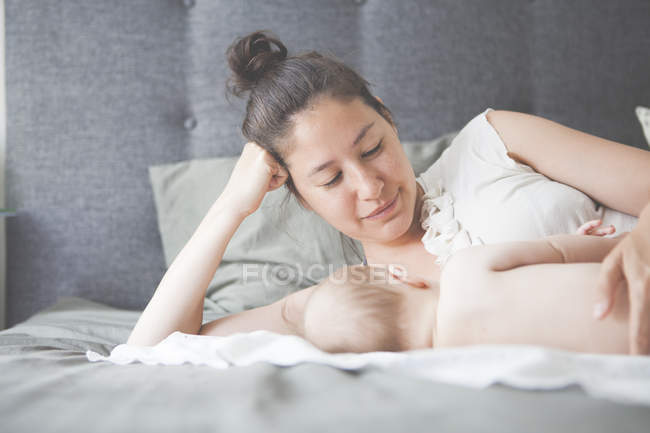 Porträt einer Mutter, die ihr Baby auf dem Bett liegend und lächelnd hält — Stockfoto