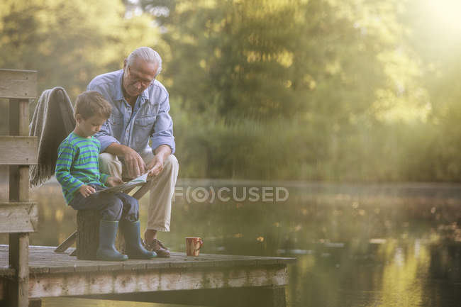 Nonno e nipote che leggono al lago — Foto stock