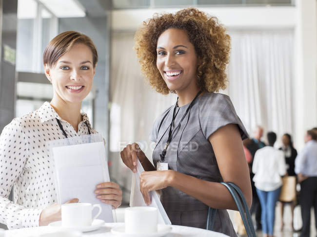 Portrait of two smiling women standing in lobby of conference center during coffee break — Stock Photo