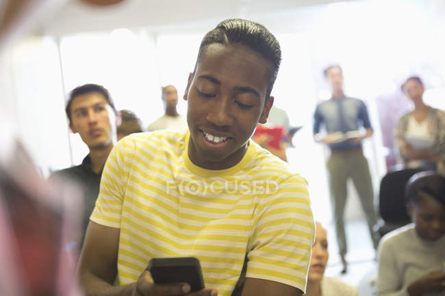 University student texting in classroom, people standing in background — Stock Photo