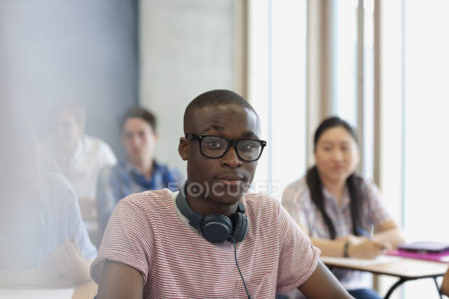 Студент-мужчина в очках и наушниках вокруг шеи смотрит в камеру во время лекции — стоковое фото