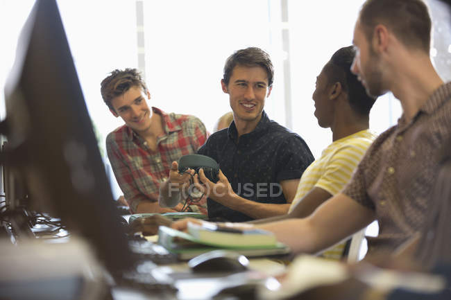 Group of smiling male students sitting at desks with computers and talking — Stock Photo