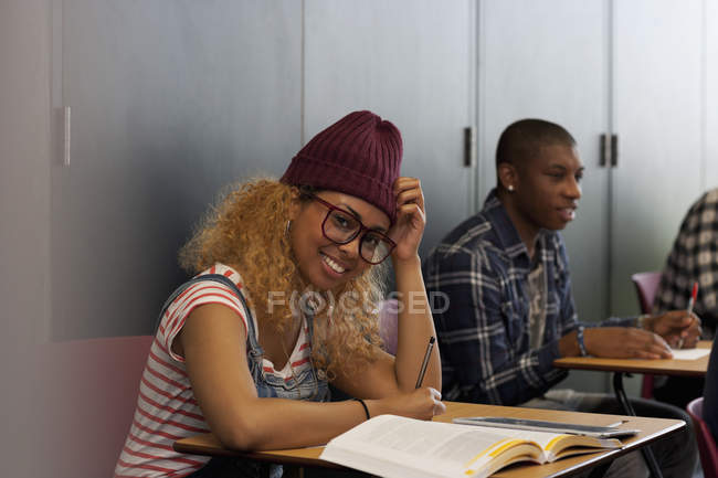 Estudiante sentada en el escritorio durante la conferencia y sonriendo a la cámara - foto de stock