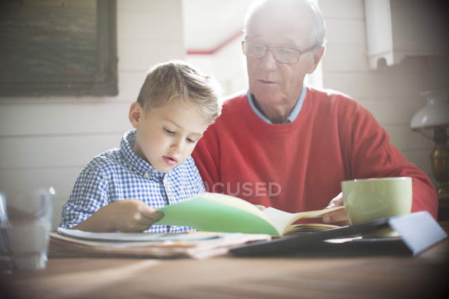 Glücklicher Junge liest mit Opa am Tisch — Stockfoto