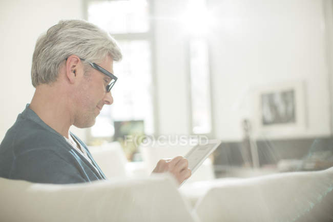 Homem mais velho usando tablet digital no sofá — Fotografia de Stock