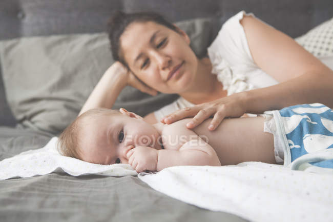 Portrait de petit bébé sucer pouce avec la mère souriant en arrière-plan — Photo de stock