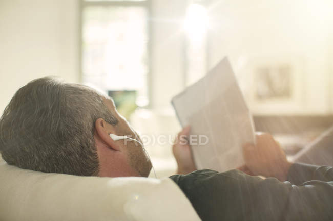 Пожилой мужчина слушает наушники на диване — стоковое фото