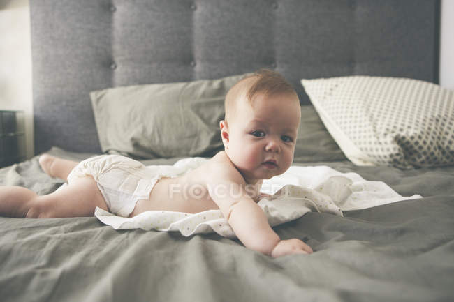 Портрет маленької дитини, що лежить спереду на ліжку з піднятою головою — стокове фото