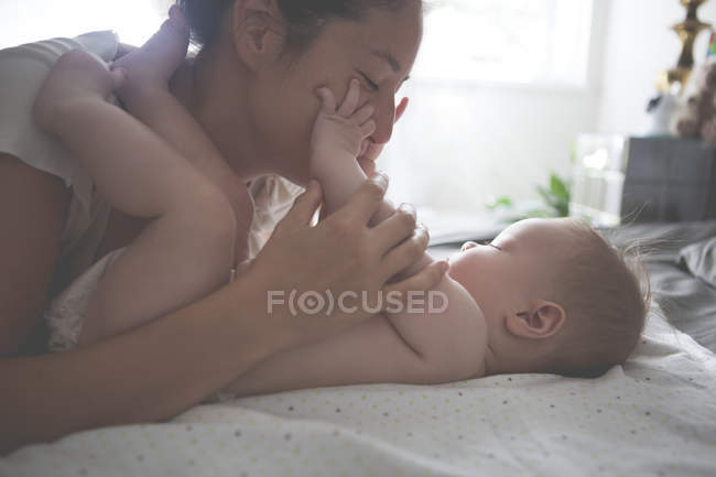 Madre jugando con el pequeño bebé, sosteniendo y besando las manos del bebé - foto de stock