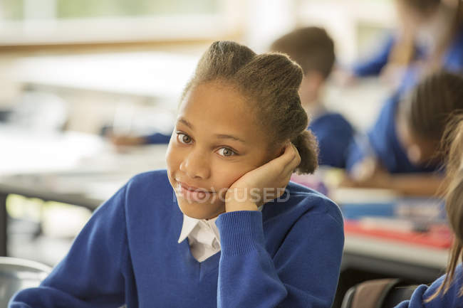 Retrato de la niña sonriente de la escuela primaria sentada aburrida en el aula - foto de stock