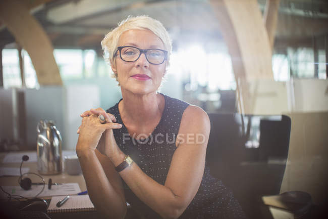 Бізнес-леді, сидячи з руками, затиснуті за офісним столом — стокове фото