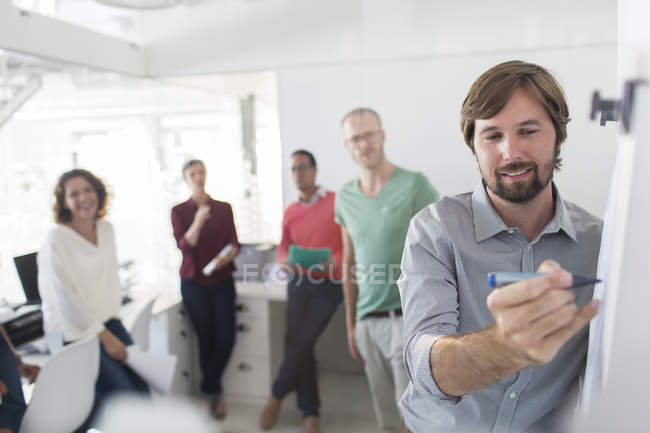 Group of people having meeting in office, man writing on flipchart — Stock Photo