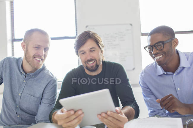 Tres hombres sonrientes trabajando con una tableta digital en la oficina - foto de stock