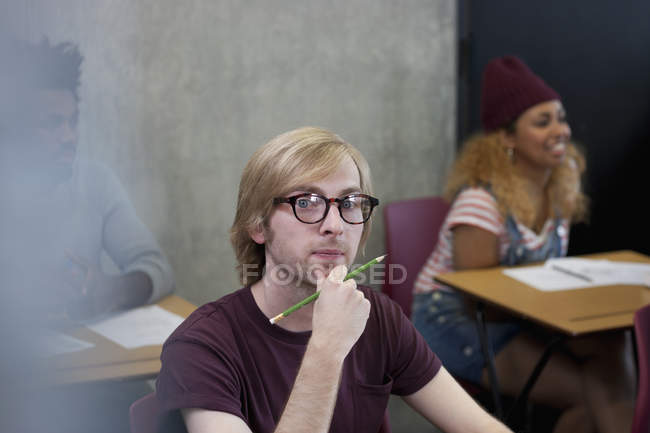 Retrato de estudante universitário sentado na mesa com a mão no queixo — Fotografia de Stock