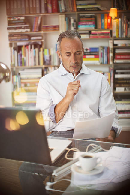 Businessman reading paperwork at home office desk — Stock Photo