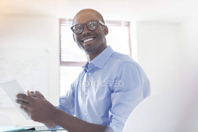 Retrato de jovem empresário vestindo óculos e camisa azul segurando tablet digital no escritório — Fotografia de Stock