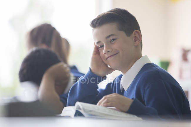 Portrait of smiling elementary school boy sitting at desk in classroom — Stock Photo