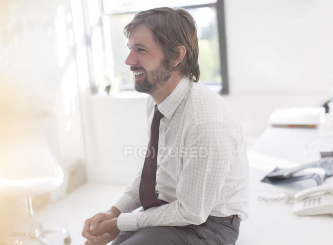 Homme d'affaires souriant portant chemise et cravate assis sur le bureau dans le bureau — Photo de stock
