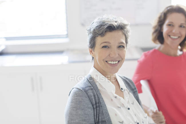 Портрет улыбающейся зрелой предпринимательницы с коллегой на заднем плане — стоковое фото
