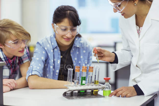 Вчитель і студенти під час уроку хімії, одягнені в захисні окуляри і дивляться на пробірки — стокове фото