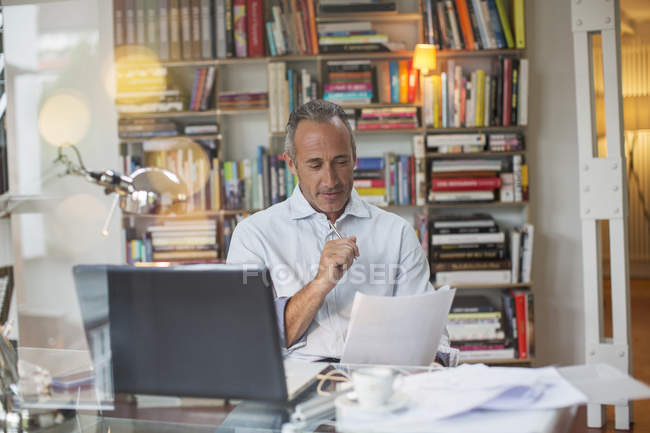 Businessman reading paperwork at home office desk — Stock Photo