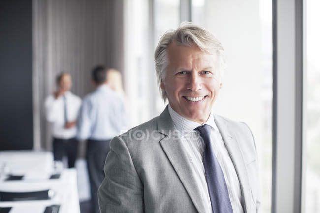 Retrato de homem de negócios em pé na sala de conferências com colegas de fundo — Fotografia de Stock