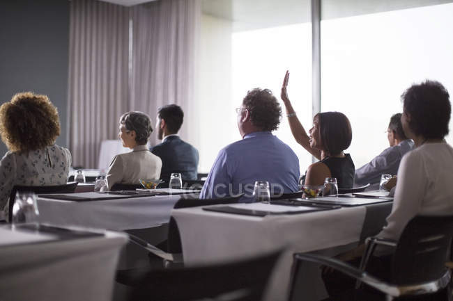 Gruppo medio di partecipanti alla conferenza seduti in sala conferenze con la mano alzata della donna — Foto stock