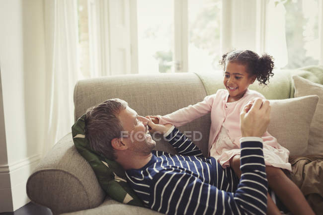 Afectuoso padre multiétnico y su hija tomados de la mano en el sofá - foto de stock
