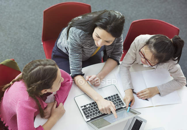 Professora ajudando meninas estudantes pesquisando no laptop na mesa da biblioteca — Fotografia de Stock