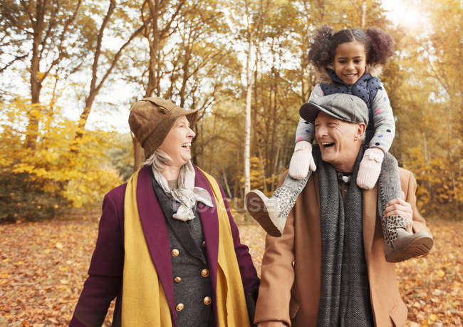 Laughing senior couple carrying daughter on shoulders in autumn woods — Stock Photo