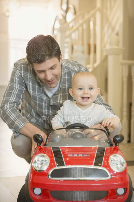 Pai empurrando feliz, bonito bebê filho no carro de brinquedo — Fotografia de Stock