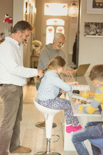 Gay father braiding daughter hair at kitchen counter — Stock Photo