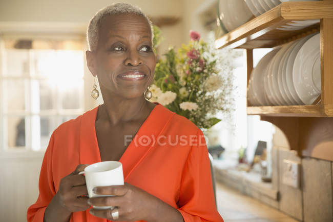 Улыбающаяся пожилая женщина пьет кофе на кухне — стоковое фото