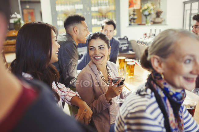 Mujeres sonrientes amigas hablando y bebiendo vino en el bar - foto de stock