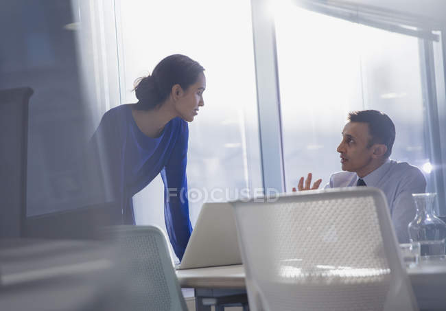 Empresario y mujer de negocios usando portátil, hablando en la oficina - foto de stock