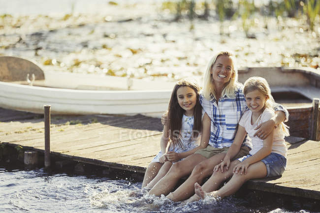 Retrato mãe feliz e filhas na doca salpicando os pés no lago — Fotografia de Stock