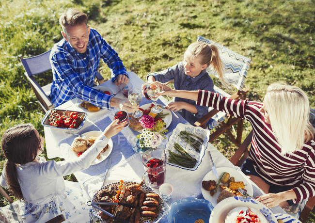 Bicchieri famiglia tostatura vino e acqua al tavolo soleggiato patio pranzo — Foto stock