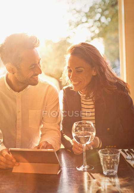 Casal jovem bebendo vinho branco e usando tablet digital no café — Fotografia de Stock
