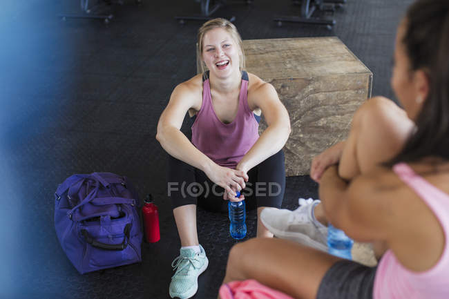 Sonrientes mujeres jóvenes riendo y hablando, bebiendo agua después del entrenamiento - foto de stock