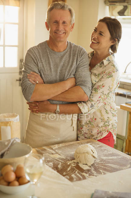 Sonriente pareja cariñosa abrazos, hornear en la cocina - foto de stock