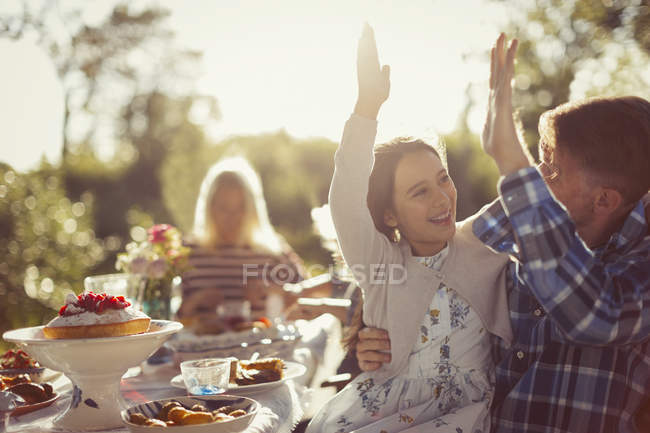 Padre giocoso e figlia che danno il cinque al soleggiato tavolo del patio della festa in giardino — Foto stock